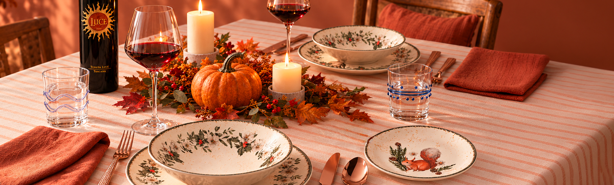Tavola autunnale con vino, calici, candele, zucca e servizio di piatti decorato