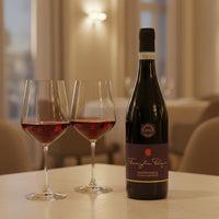 Bottiglia di vino rosso Valpolicella Famiglia Pasqua 2021 accanto a due calici con vino rosso su tavolo chiaro in ambiente interno elegante.